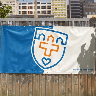 Bauzaunbanner mit Logo des Allgemeinen Krankenhauses Celle und Webadresse akh-celle.de/zukunft vor städtischer Kulisse