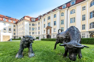Außenansicht des Denkströme-Büros in München: helles, historisches Gebäude mit rotem Dach; im Vordergrund stehen bronzene Statuen von Bär und Stier im Innenhof.