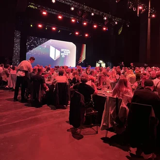 Blick in die festliche Veranstaltungshalle des German Brand Award 2025 in Berlin: Zahlreiche Gäste aus Marketing, Wirtschaft und Medien sitzen an elegant gedeckten Tischen, während auf der Bühne die Preisverleihung unter stimmungsvollem Licht stattfindet.