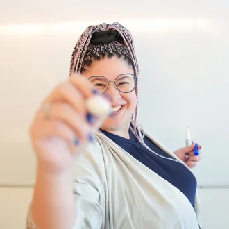 Mitarbeiterin aus der Grafikabteilung von Denkströme steht vor einem Whiteboard, lächelt in die Kamera und hält einen Whiteboard-Marker in der Hand.