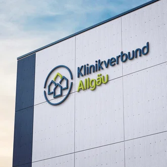 Fassadenbeschriftung mit dem blau-grünen Logo des Klinikverbunds Allgäu