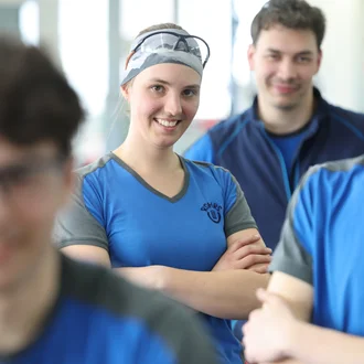 Junge Mitarbeitende der Dr. Werner Röhrs GmbH & Co. KG stehen lächelnd in Arbeitskleidung in einer Produktionshalle – Fokus auf Teamgeist, Nachwuchsförderung und modernes Arbeitsumfeld im technischen Bereich.