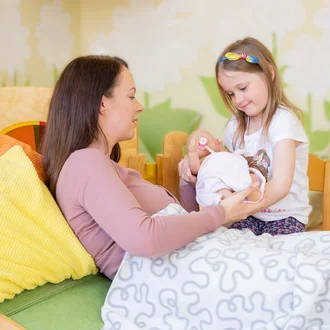 Kind mit Babypuppe spielt Geburtssituation mit erwachsener Frau nach – gefühlvolles Motiv zur Berufsorientierung für angehende Hebammen im Klinikverbund Allgäu.