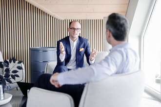 Beratungsgespräch bei Denkströme: Ein Manager im Anzug erklärt gestikulierend etwas in einem Lounge-Bereich, gegenüber sitzt ein Gesprächspartner.