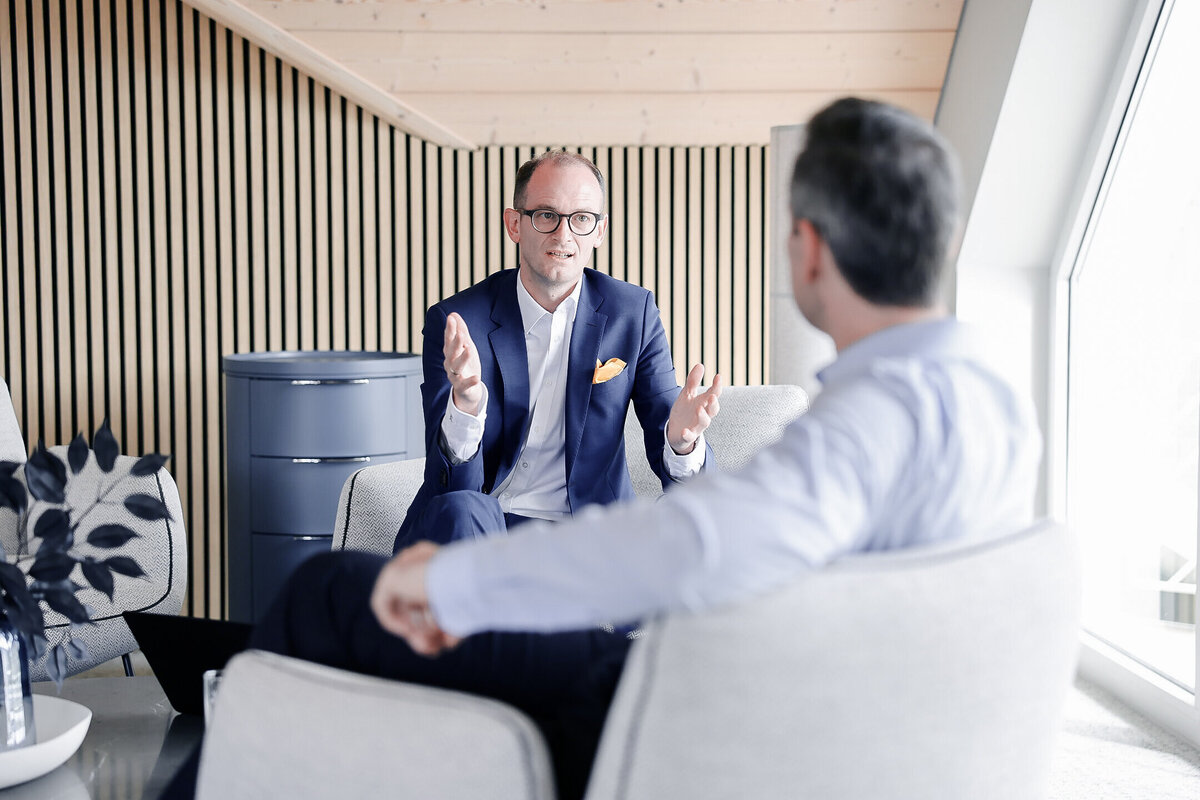 Beratungsgespräch bei Denkströme: Ein Manager im Anzug erklärt gestikulierend etwas in einem Lounge-Bereich, gegenüber sitzt ein Gesprächspartner.