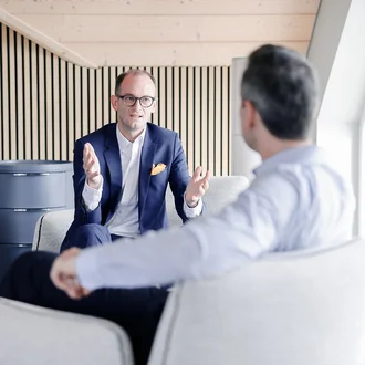 Beratungsgespräch bei Denkströme: Ein Manager im Anzug erklärt gestikulierend etwas in einem Lounge-Bereich, gegenüber sitzt ein Gesprächspartner.