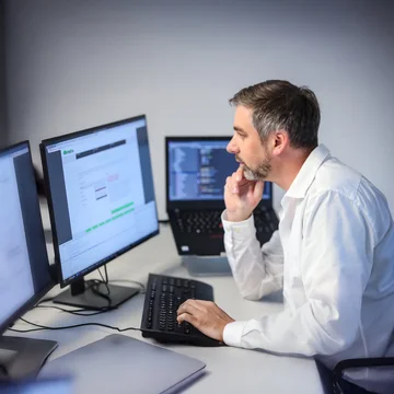 Denkströme IT-Spezialist arbeitet konzentriert an mehreren Monitoren – Softwareentwicklung und Programmierung im modernen Büro