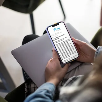Frau liest auf einem Smartphone eine Pressemitteilung des VPKA – Verband der Privatkliniken in Bayern e. V. – mit dem Titel „Von der Notaufnahme in die Psychosomatik“ – digitale Kommunikation im Gesundheitswesen zu Themen rund um Versorgung und Rehabilitation.