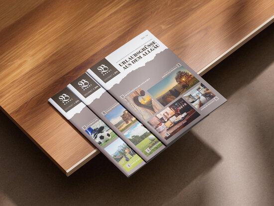 Drei Ausgaben des Urlaubsmagazins „Urlaubsgrüße aus dem Allgäu“ vom Parkhotel Burgmühle auf Holztisch, mit Titelseiten zu saisonalen Themen