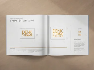 Geöffnetes Markenhandbuch auf einem Holztisch mit Designrichtlinien zu Schutzraum und Mindestgröße des DENKSTRÖME-Logos – zeigt professionelles Corporate Design und visuelle Markenführung