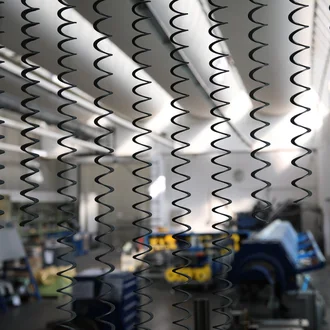 Große technische Wellenfedern der Dr. Werner Röhrs GmbH & Co. KG hängen in einer hellen Fertigungshalle – Fokus auf industrielle Präzision, Federtechnologie und moderne Produktion in der Metallverarbeitung.