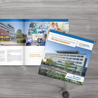 Aufgeschlagene Imagebroschüre des Allgemeinen Krankenhauses Celle mit Klinikansichten, medizinischen Szenen und dem Claim „Für Ihre Gesundheit“