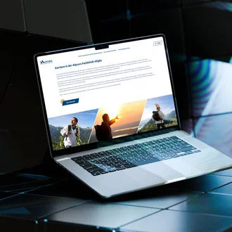 Laptop auf reflektierendem Untergrund zeigt Karrierewebseite der Alpcura Fachklinik Allgäu mit Stellenangeboten und Naturmotiven im Header.