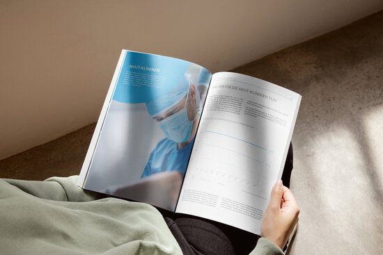 Person liest eine geöffnete Broschüre des VPKA mit dem Thema „Akut-Kliniken“ – linke Seite zeigt einen operierenden Arzt mit Mundschutz, rechte Seite informiert über Leistungen für Akutkliniken mit Text und Diagramm – hochwertige Gesundheitskommunikation im Printformat.