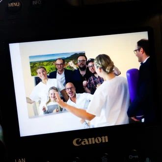 Gruppenfoto von fröhlichem Klinikteam und Kind auf Kamera-Display, aufgenommen bei einem Fotoshooting in medizinischem Umfeld.