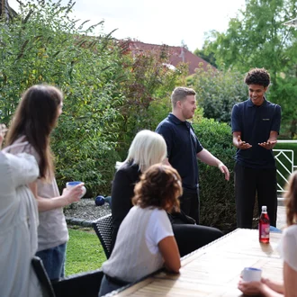 Team von Denkströme auf der Terrasse in Kempten: Mitarbeitende stehen und sitzen um einen Tisch, tauschen sich aus und trinken Kaffee im Gartenbereich.