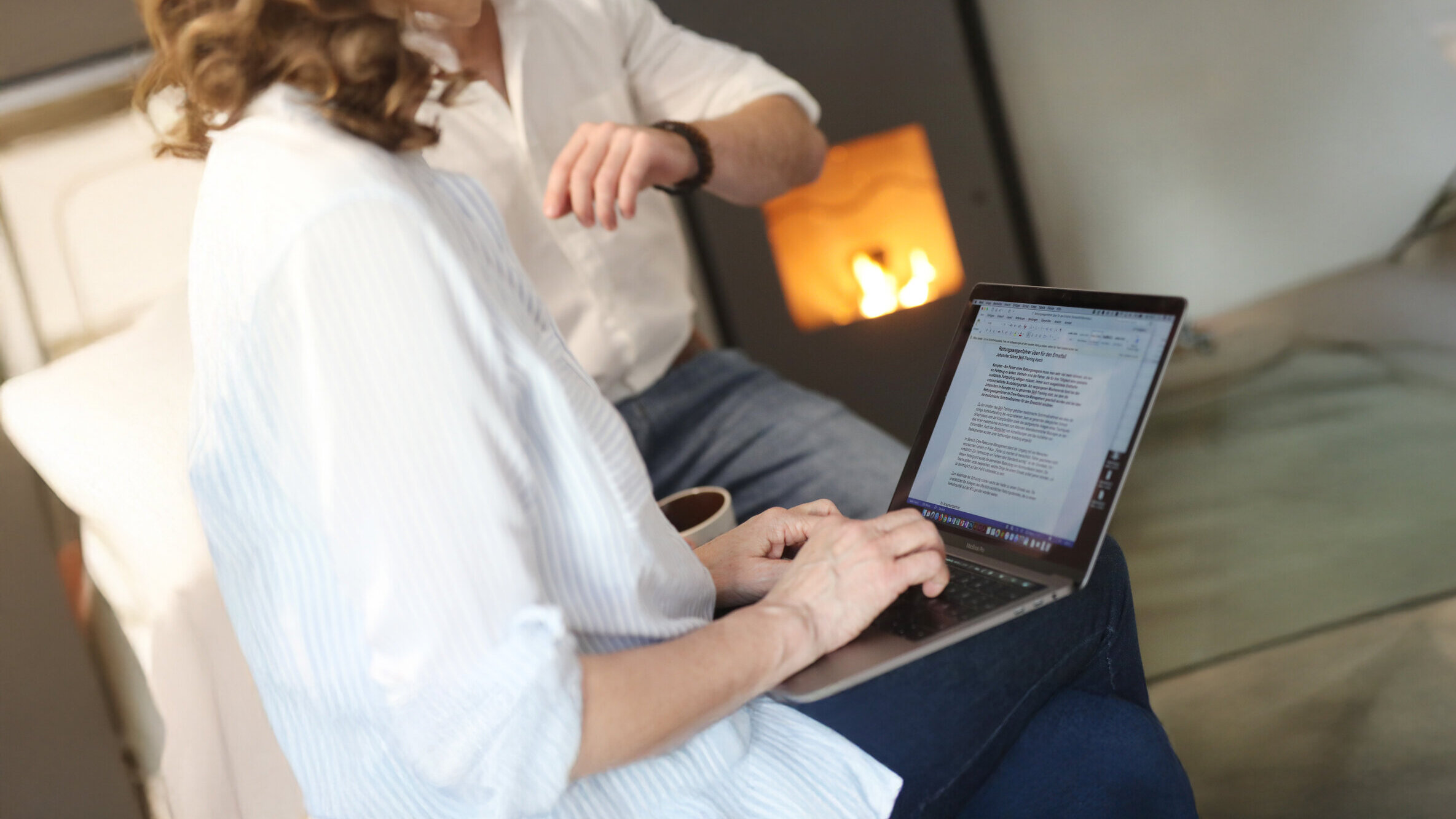 Frau arbeitet mit Laptop im gemütlichen Raum mit Kamin 