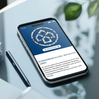 Smartphone liegt auf einem Glastisch und zeigt die Karrierestartseite des Klinikverbunds Allgäu mit Logo, Button „Zu den Stellen“ und einleitendem Text.