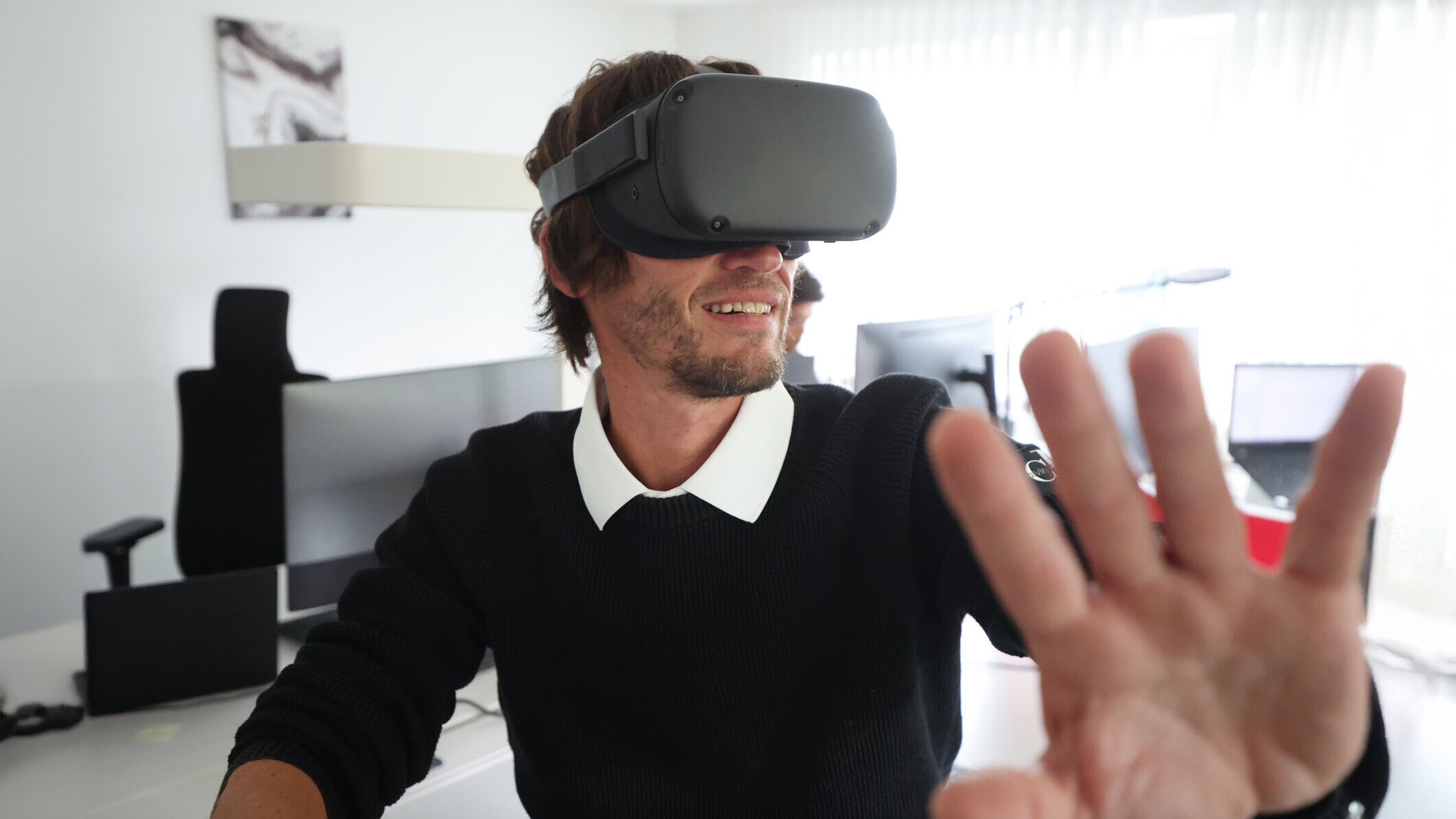 Mitarbeiter aus dem Technikteam von Denkströme testet eine VR-Brille im Büro und streckt die Hand nach vorn, als würde er virtuelle Elemente bedienen.