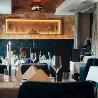 Stimmungsvolles Hotelrestaurant mit dunklen Polsterstühlen, Kerzenschein, Holzverkleidung und Winterdeko in Alpenoptik