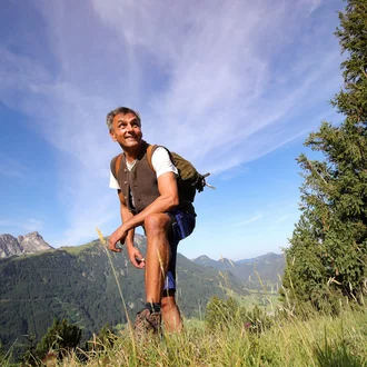 Technischer Mitarbeiter in traditioneller Weste auf einem Berg mit Blick ins Tal – authentisches Porträt für Handwerksberufe im Klinikalltag der Fachklinik Allgäu.