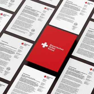 Layout-Entwurf mit Pressemitteilungen des Bayerischen Roten Kreuzes auf stilisiertem Hintergrund – Mockup für Öffentlichkeitsarbeit, Corporate Design und PR-Kommunikation