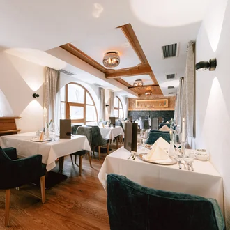 Elegantes Hotelrestaurant mit weißen Tischdecken, Holzdecke, großen Rundbogenfenstern und stilvoller Alpen-Deko