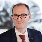 Portrait von Fabian Schmid, Geschäftsführer der Denkströme Gruppe, im Business-Outfit mit roter Krawatte – moderne Führungspersönlichkeit im Bereich Kommunikation und Transformation