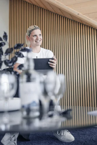 Teresa Schmid von Denkströme sitzt im Besprechungsraum und hält ein Tablet in den Händen; im Vordergrund stehen unscharf Wasserflasche und Gläser auf dem Konferenztisch.