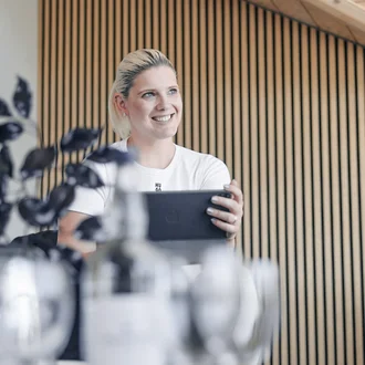 Teresa Schmid von Denkströme sitzt im Besprechungsraum und hält ein Tablet in den Händen; im Vordergrund stehen unscharf Wasserflasche und Gläser auf dem Konferenztisch.
