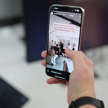 Hand hält ein Smartphone mit geöffneter Denkströme-Instagram-Story; auf dem Display ist ein Behind-the-Scenes-Foto eines Teamshootings im Büro zu sehen.