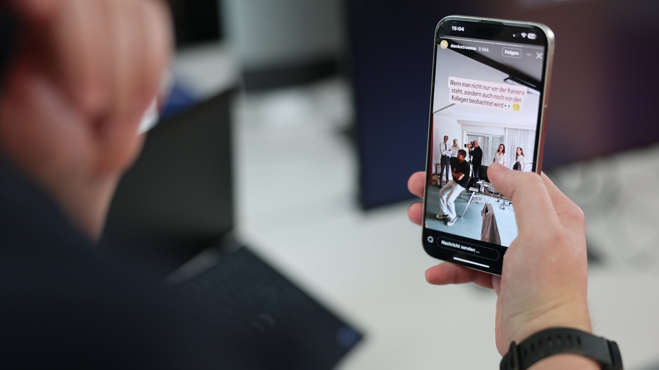 Hand hält ein Smartphone mit geöffneter Denkströme-Instagram-Story; auf dem Display ist ein Behind-the-Scenes-Foto eines Teamshootings im Büro zu sehen.