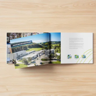 Geöffnete Ausbildungsbroschüre von EK-Pack Folien auf hellem Holztisch – linke Seite mit Luftbild der Produktionsstätte inmitten grüner Landschaft, Text „Dürfen wir uns vorstellen?“; rechte Seite mit Vorstellungstext des Unternehmens und Icons zu Lebensmittel-, Medizin- und Technikbranchen