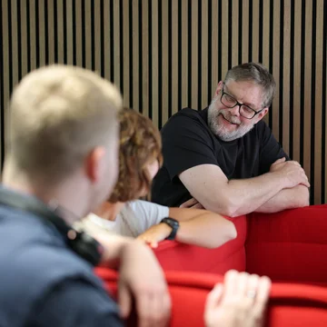 Denkströme Team im Gespräch in der roten Lounge im Büro; ein Mitarbeiter lehnt an der Sitzbank und diskutiert mit Kolleginnen und Kollegen zur Social-Media-Strategie.