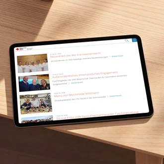 Tablet auf hellem Holztisch zeigt die Presseseite des Bayerischen Roten Kreuzes mit Artikeln über Neuwahlen, Ehrenamt und Veranstaltungen – digitale Öffentlichkeitsarbeit und moderne Informationsvermittlung