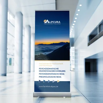 Roll-up-Display der Alpcura Fachklinik Allgäu mit Bergmotiv und Informationen zu Psychosomatik und Pneumologie in moderner Eingangshalle.