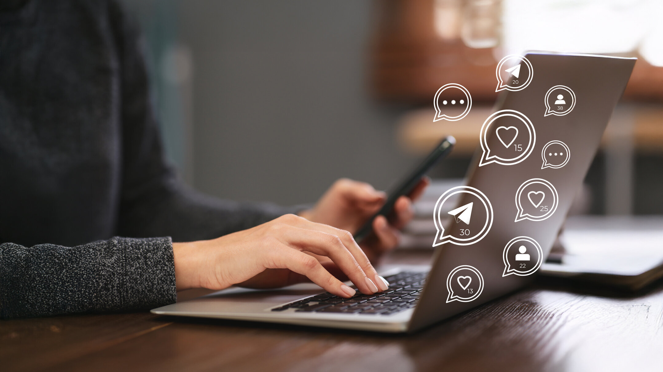 Person tippt auf einem Laptop und hält ein Smartphone, umgeben von digitalen Symbolen für Likes, Nachrichten und Follower