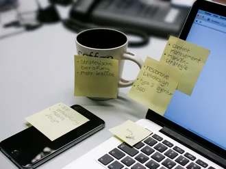 Nahaufnahme eines modernen Arbeitsplatzes bei der Denkströme mit Laptop, Smartphone, Kaffeetasse und vielen Post-its mit Aufgaben zu Webdesign, SEO, Content und Markenstrategie 
