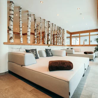 Moderner Wellnessbereich mit hellen Relaxliegen, Naturholzdekor und Birkenstämmen in alpinem Designambiente