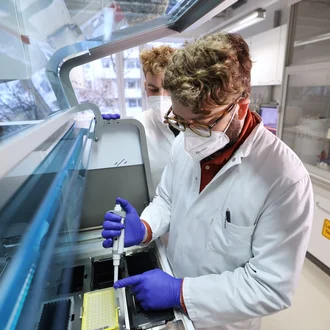 Labormitarbeitende im DHZM arbeiten konzentriert mit moderner Analyse-Technik – Pipettieren unter Sicherheitsvorkehrungen im Diagnostiklabor