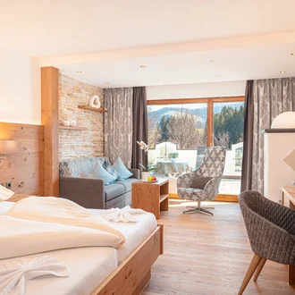 Helles Alpenhotelzimmer mit Holzboden, gemütlicher Sitzecke, Balkonblick auf Berge und modernem Interieur im Landhausstil