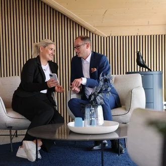 Geschäftsleitung von Denkströme im Gespräch: Zwei Führungskräfte sitzen in einem Lounge-Bereich, schauen auf ein Smartphone und besprechen Inhalte.