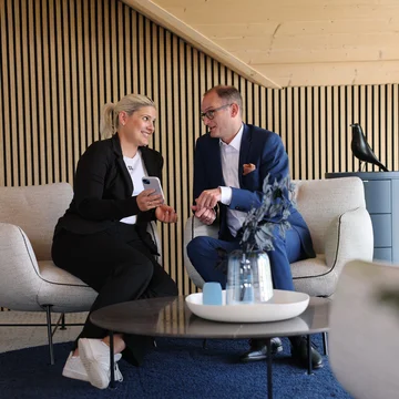 Geschäftsleitung von Denkströme im Gespräch: Zwei Führungskräfte sitzen in einem Lounge-Bereich, schauen auf ein Smartphone und besprechen Inhalte.