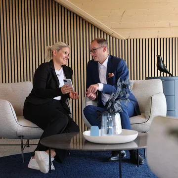 Geschäftsleitung von Denkströme im Gespräch: Zwei Führungskräfte sitzen in einem Lounge-Bereich, schauen auf ein Smartphone und besprechen Inhalte.