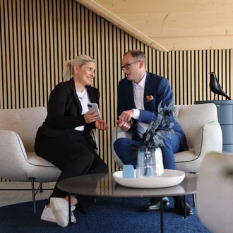 Geschäftsleitung von Denkströme im Gespräch: Zwei Führungskräfte sitzen in einem Lounge-Bereich, schauen auf ein Smartphone und besprechen Inhalte.