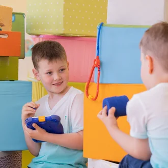 Kinder spielen Lagerlogistik zwischen bunten Kisten und medizinischem Spielzeug – kreatives Motiv zur Nachwuchsgewinnung für Lager- und Versorgungsberufe im Klinikverbund Allgäu.