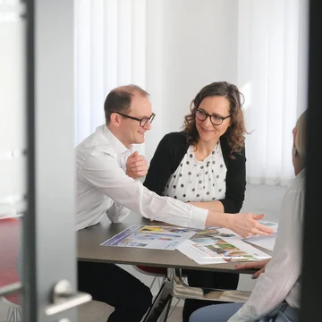 Teammeeting bei Denkströme: Drei Personen sitzen am Tisch und besprechen gedruckte Recruiting- und Kampagnenunterlagen in einem hellen Besprechungsraum.