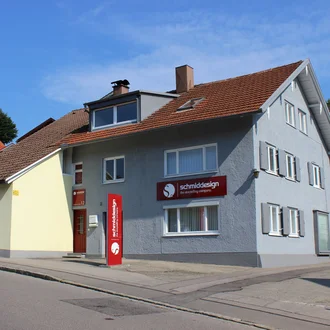 Außenansicht des Agenturgebäudes von schmiddesign mit Firmenlogo und rotem Firmenschild in sonniger Wohnlage in Kempten  im Allgäu