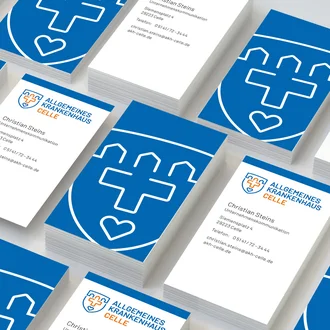 Gestapelte Visitenkarten des Allgemeinen Krankenhauses Celle mit Logo, Kontaktdaten und großflächigem Wappenmotiv in Blau und Weiß