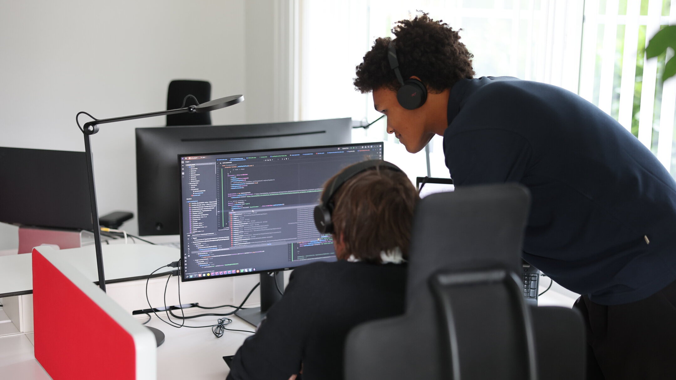 Zwei Denkströme Mitarbeitende arbeiten im Büro an der TYPO3-Website-Entwicklung und prüfen Quellcode am Monitor.